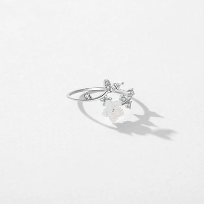 Delicate silver ring featuring a white carved flower and sparkling leaf-shaped stones arranged in a graceful, curved design.

