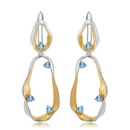 Dangling earrings with flowing gold and silver forms set with turquoise-colored stones

