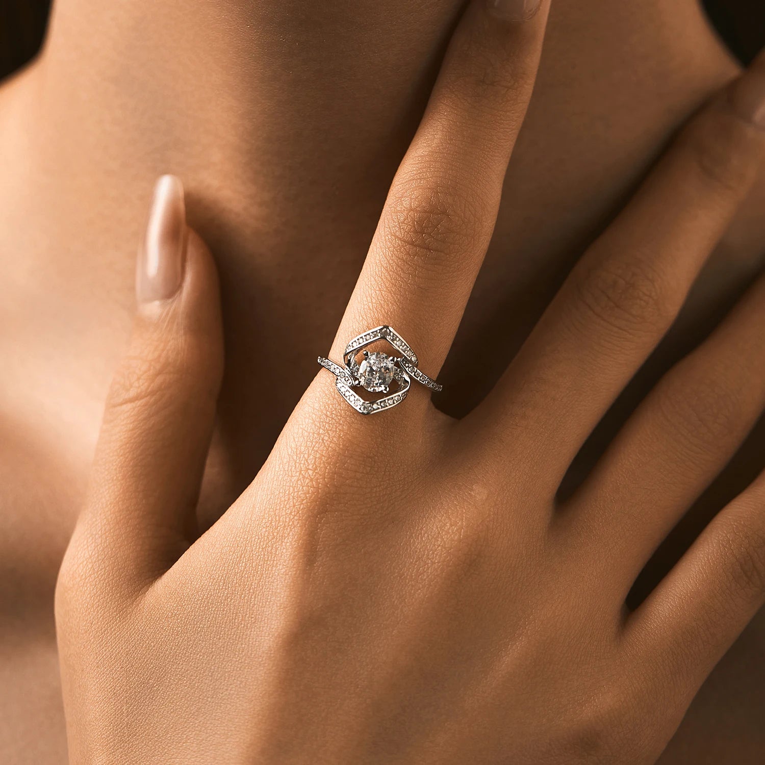 Silver ring with a central round white stone encircled by two asymmetrical open square-shaped bands encrusted with smaller stones.

