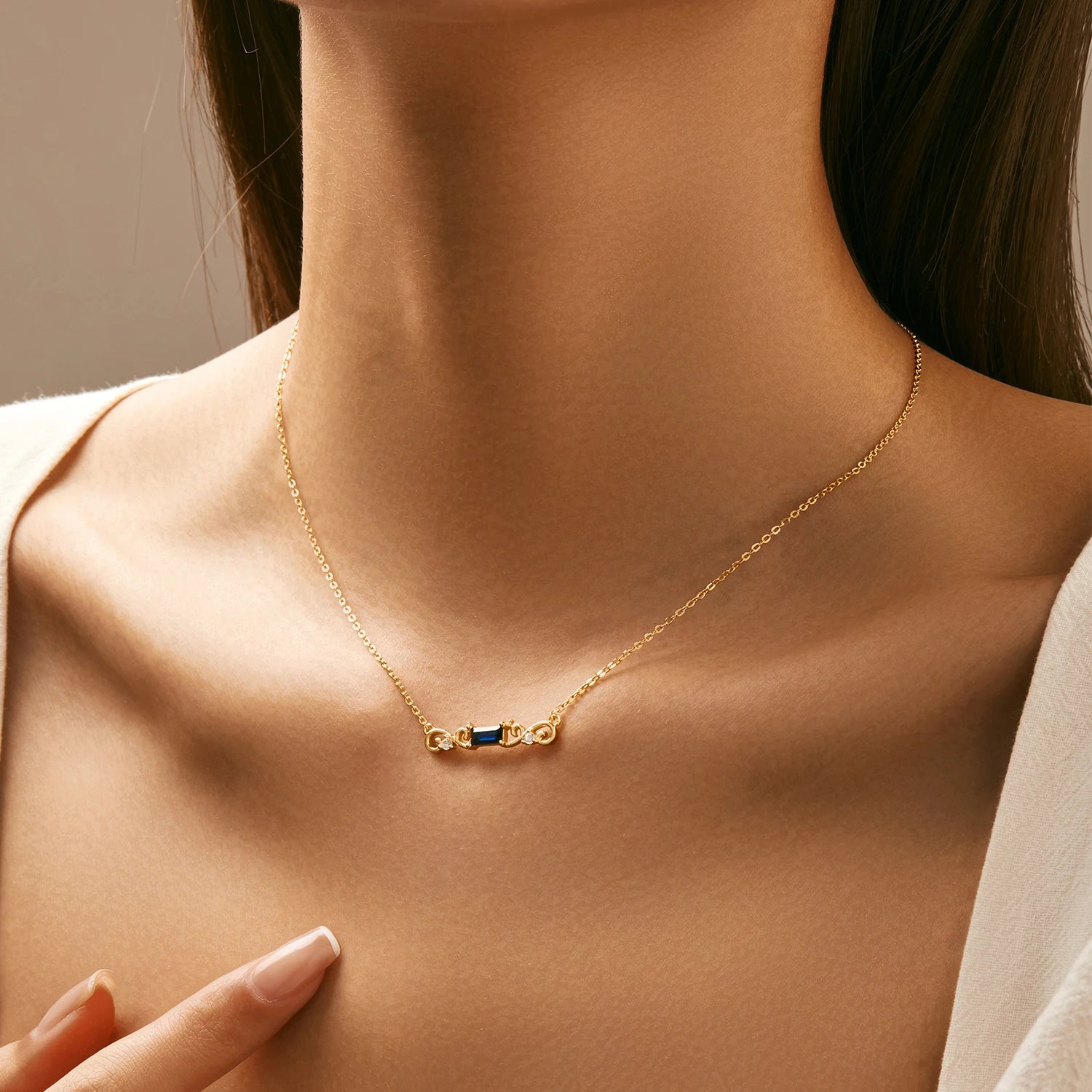 Gold necklace with a central rectangular deep blue gemstone flanked by scroll-like gold accents and small clear crystals