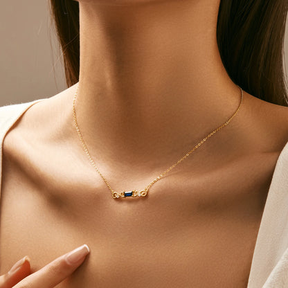 Gold necklace with a central rectangular deep blue gemstone flanked by scroll-like gold accents and small clear crystals