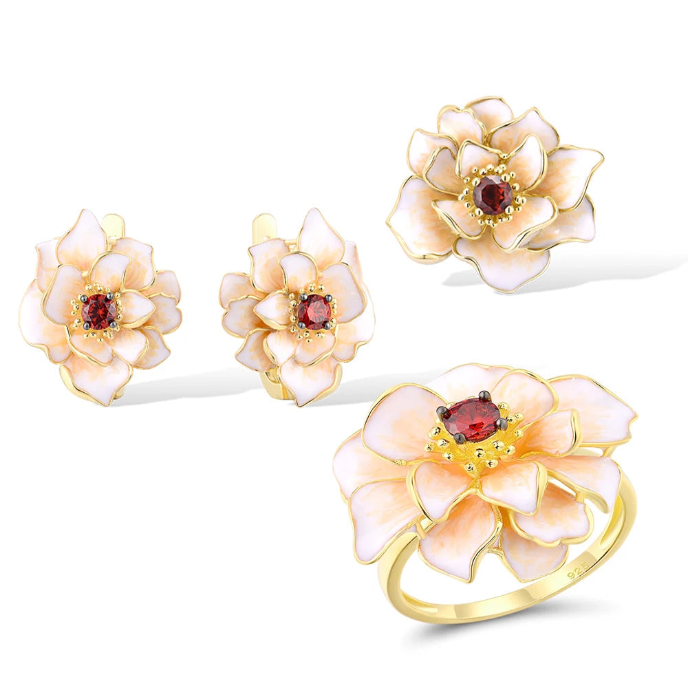 Jewelry set with white enamel floral design and red gemstone center, including a ring, earrings, and pendant.

