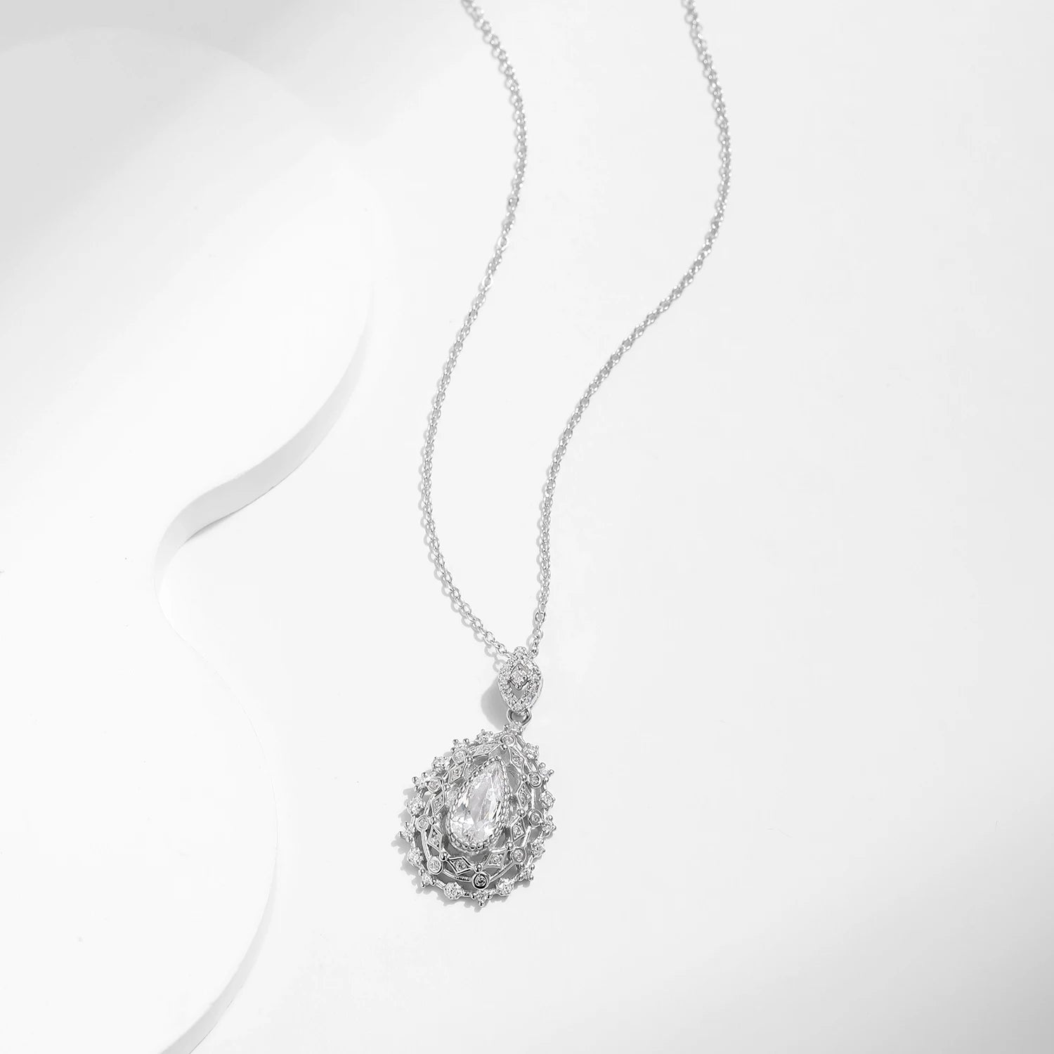 Ornate silver necklace with an intricate teardrop pendant, featuring a central pear-cut white gemstone, part of the Bianco Nero collection.

