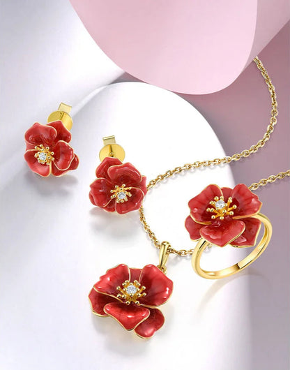 Jewelry set from the Rossa Collection featuring red enamel flower-shaped earrings, pendant, and ring with gold-tone detailing and central white stones.

