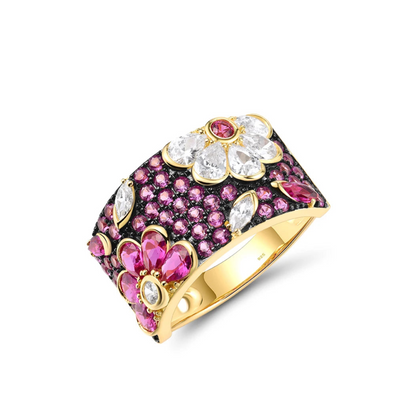 Wide gold ring adorned with vibrant pink and white gemstones arranged in floral patterns.

