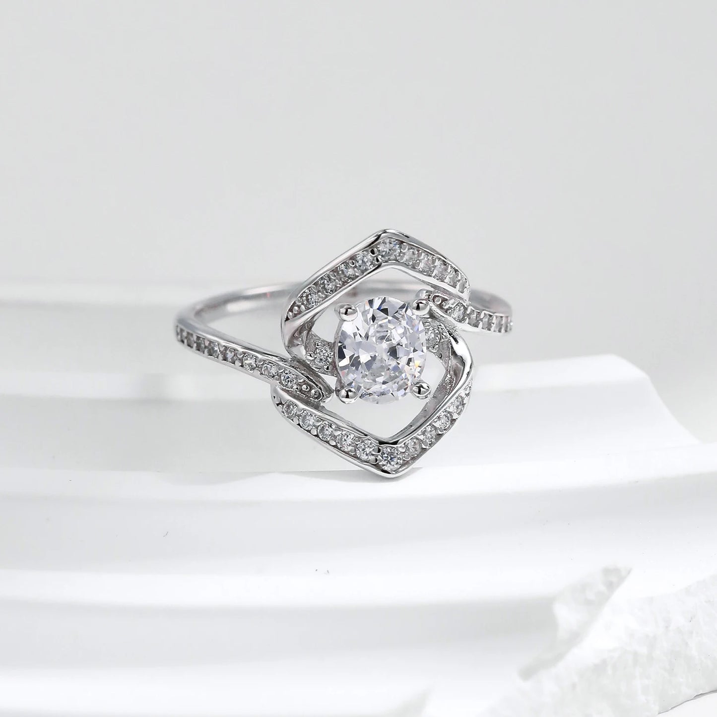 Silver ring with a central round white stone encircled by two asymmetrical open square-shaped bands encrusted with smaller stones.

