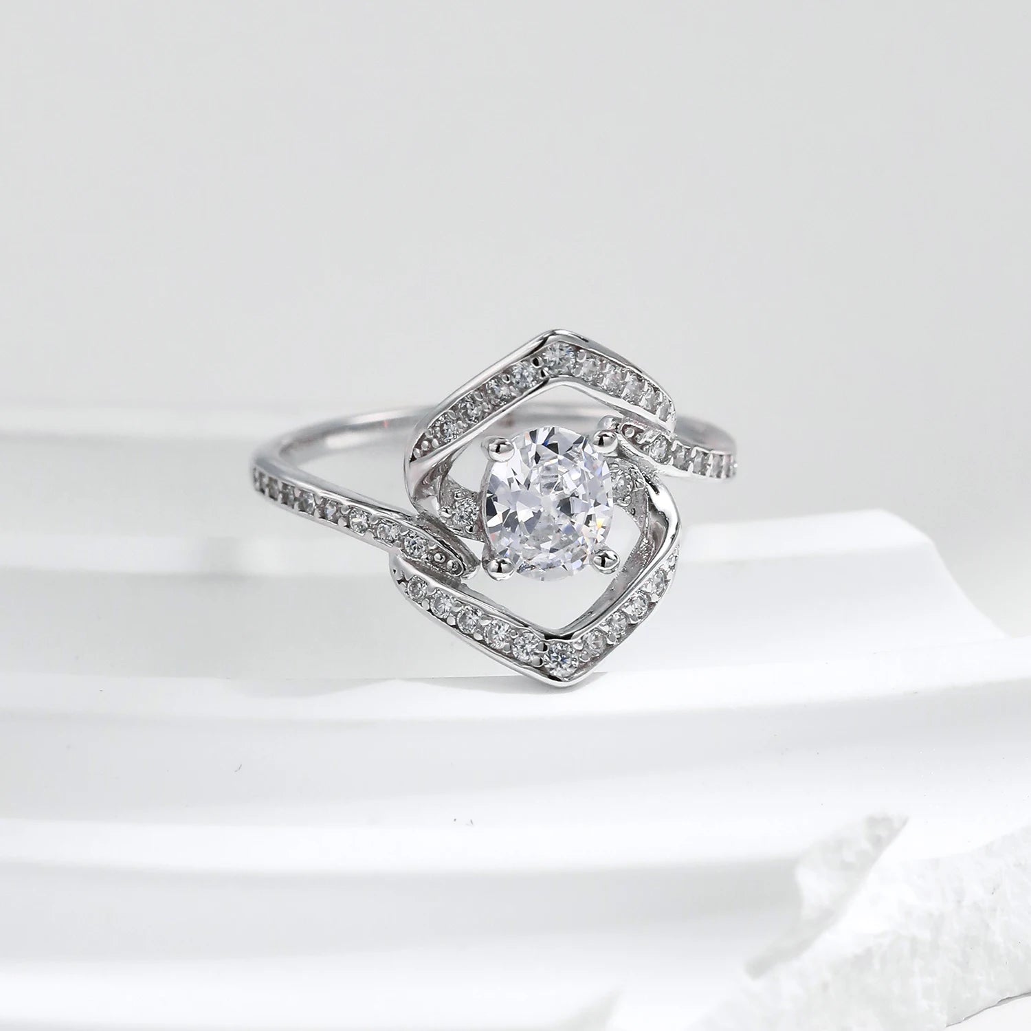 Silver ring with a central round white stone encircled by two asymmetrical open square-shaped bands encrusted with smaller stones.

