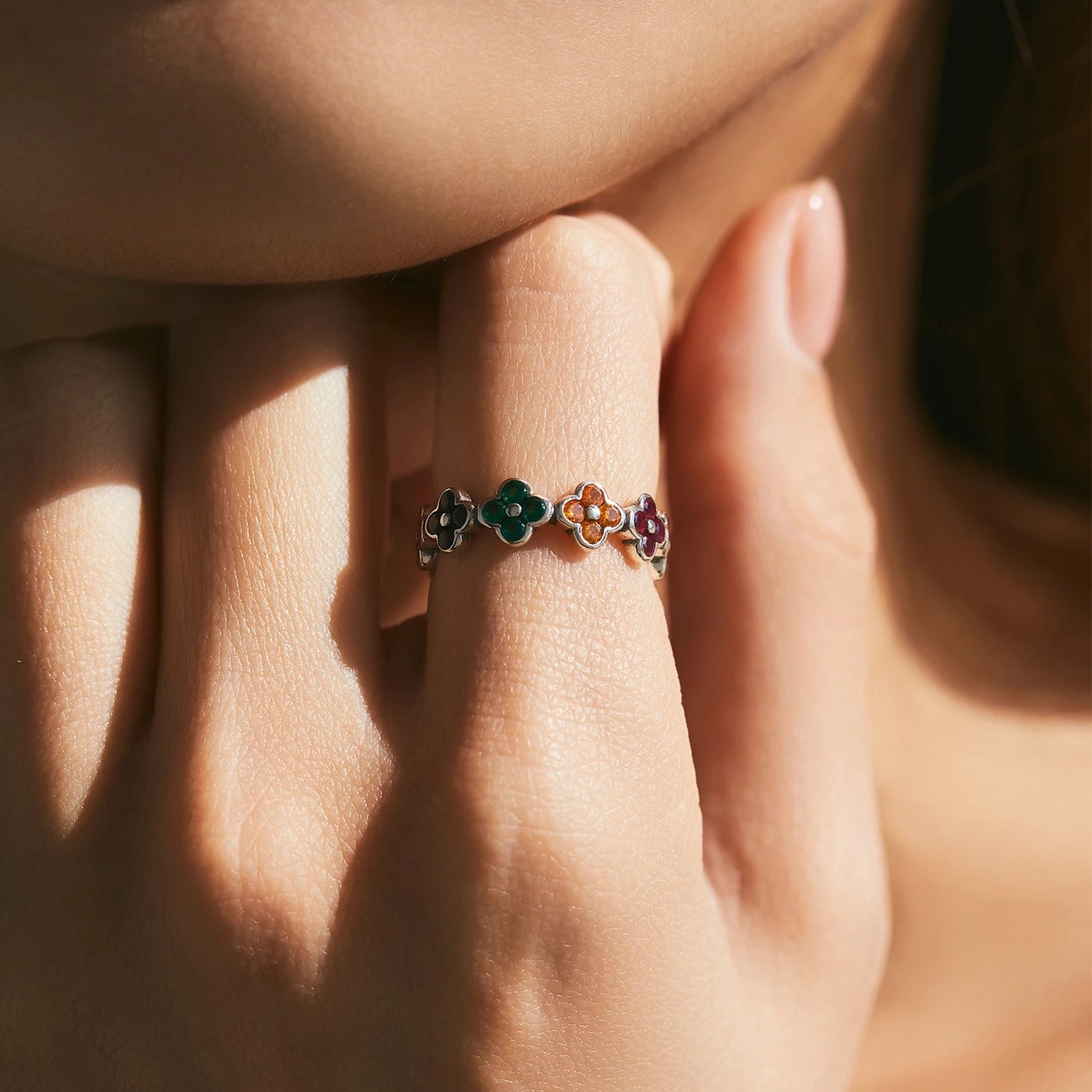 Silver ring with multicoloured four-petal flower gemstones set around the band.

