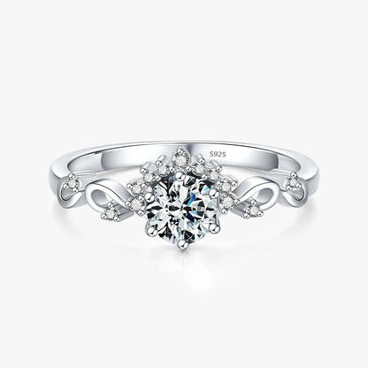 Silver ring with a central round-cut stone surrounded by delicate side diamonds and twisted vine-like detailing.

