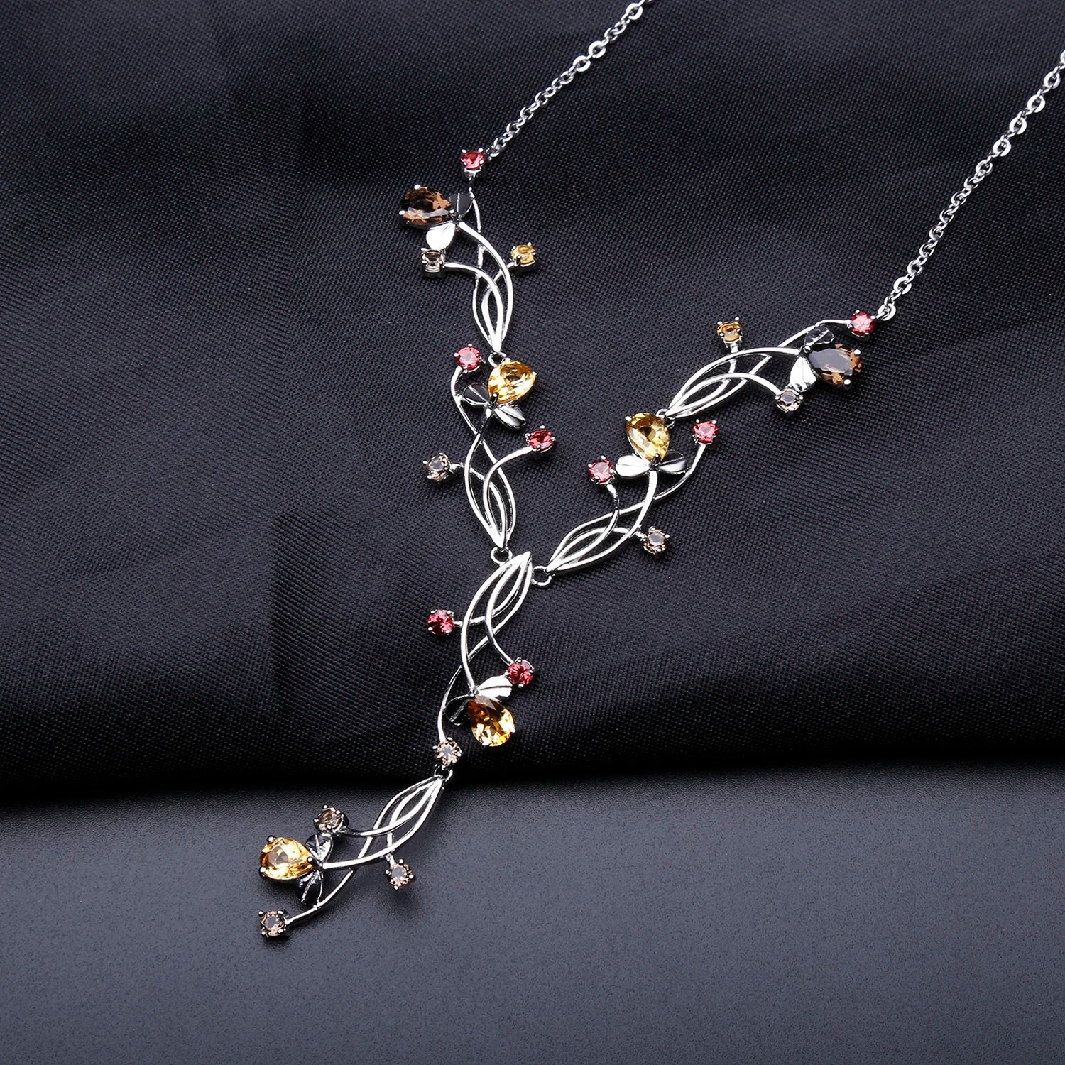 Silver necklace with an intricate swirling design, adorned with multicolored gemstones in pink, yellow, brown, and clear tones.

