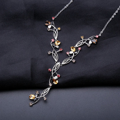 Silver necklace with an intricate swirling design, adorned with multicolored gemstones in pink, yellow, brown, and clear tones.

