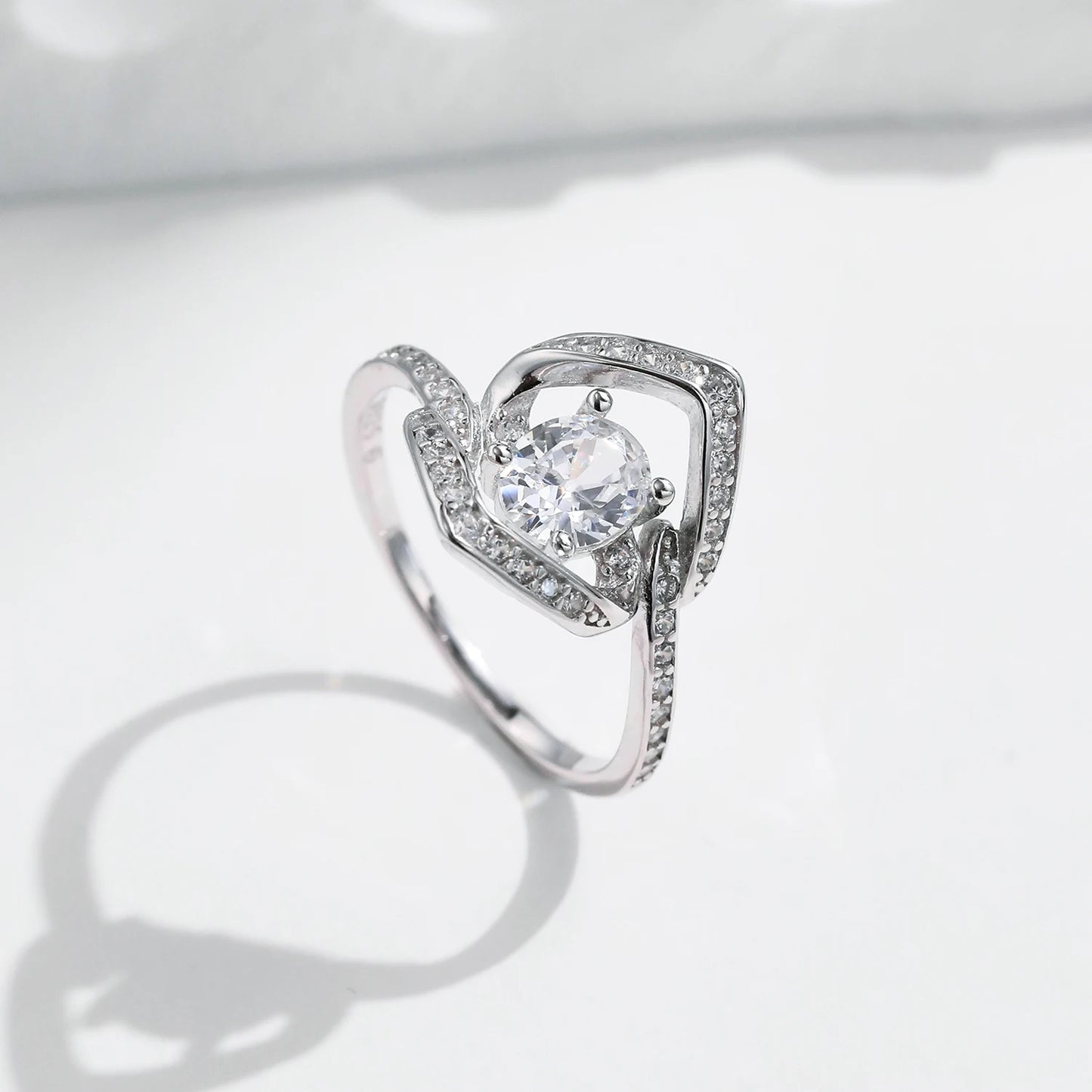 Silver ring with a central round white stone encircled by two asymmetrical open square-shaped bands encrusted with smaller stones.

