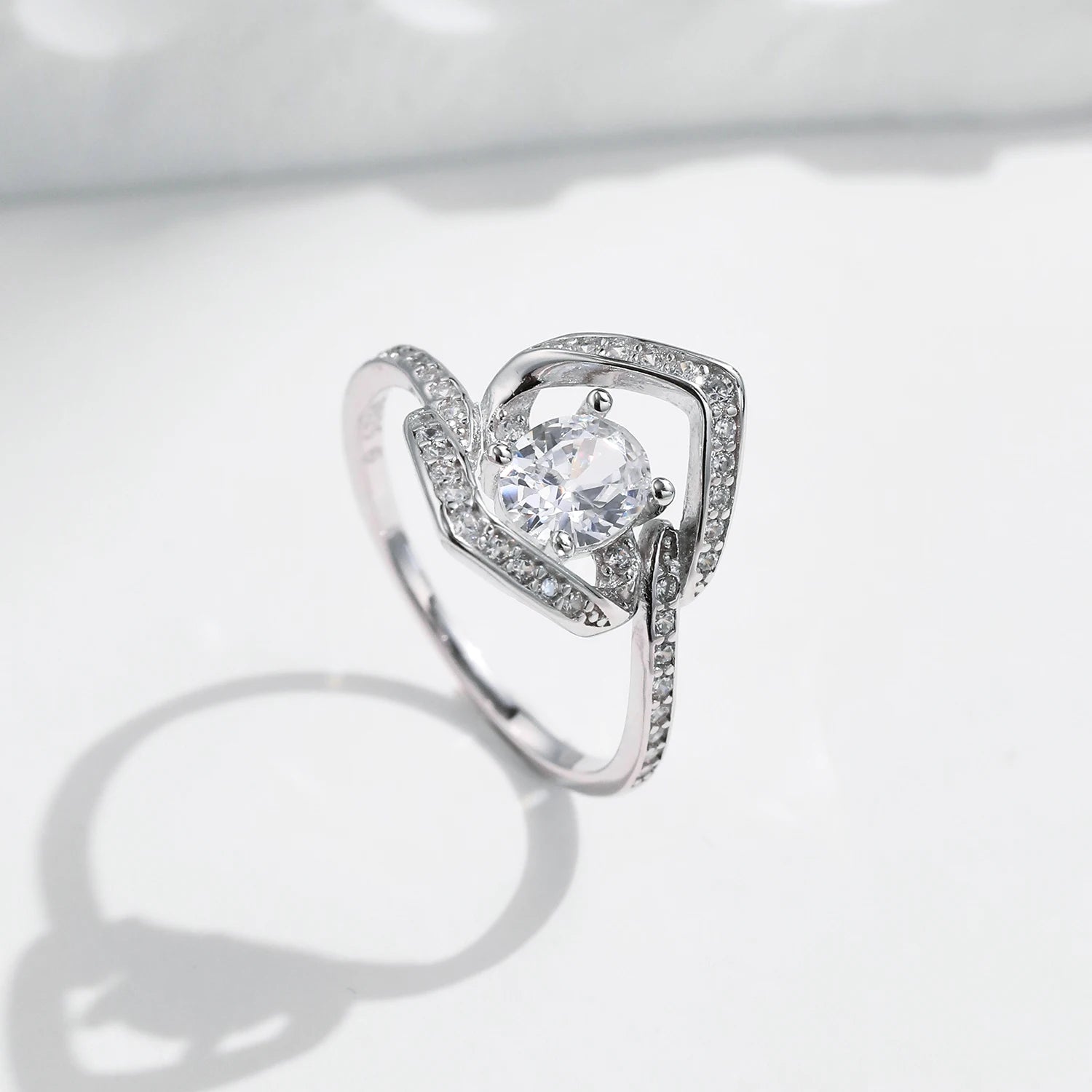 Silver ring with a central round white stone encircled by two asymmetrical open square-shaped bands encrusted with smaller stones.

