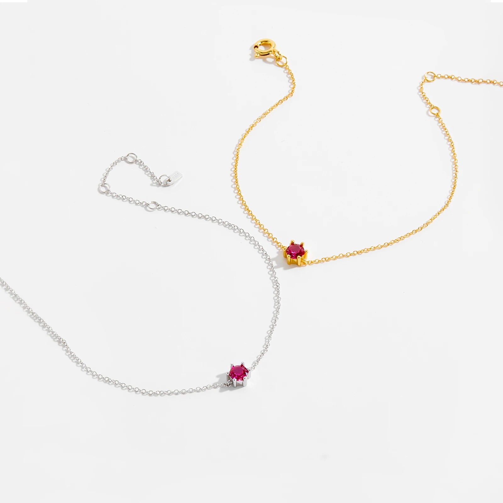 Delicate silver bracelet featuring a single round red stone set at the center.

