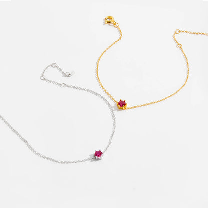 Delicate silver bracelet featuring a single round red stone set at the center.

