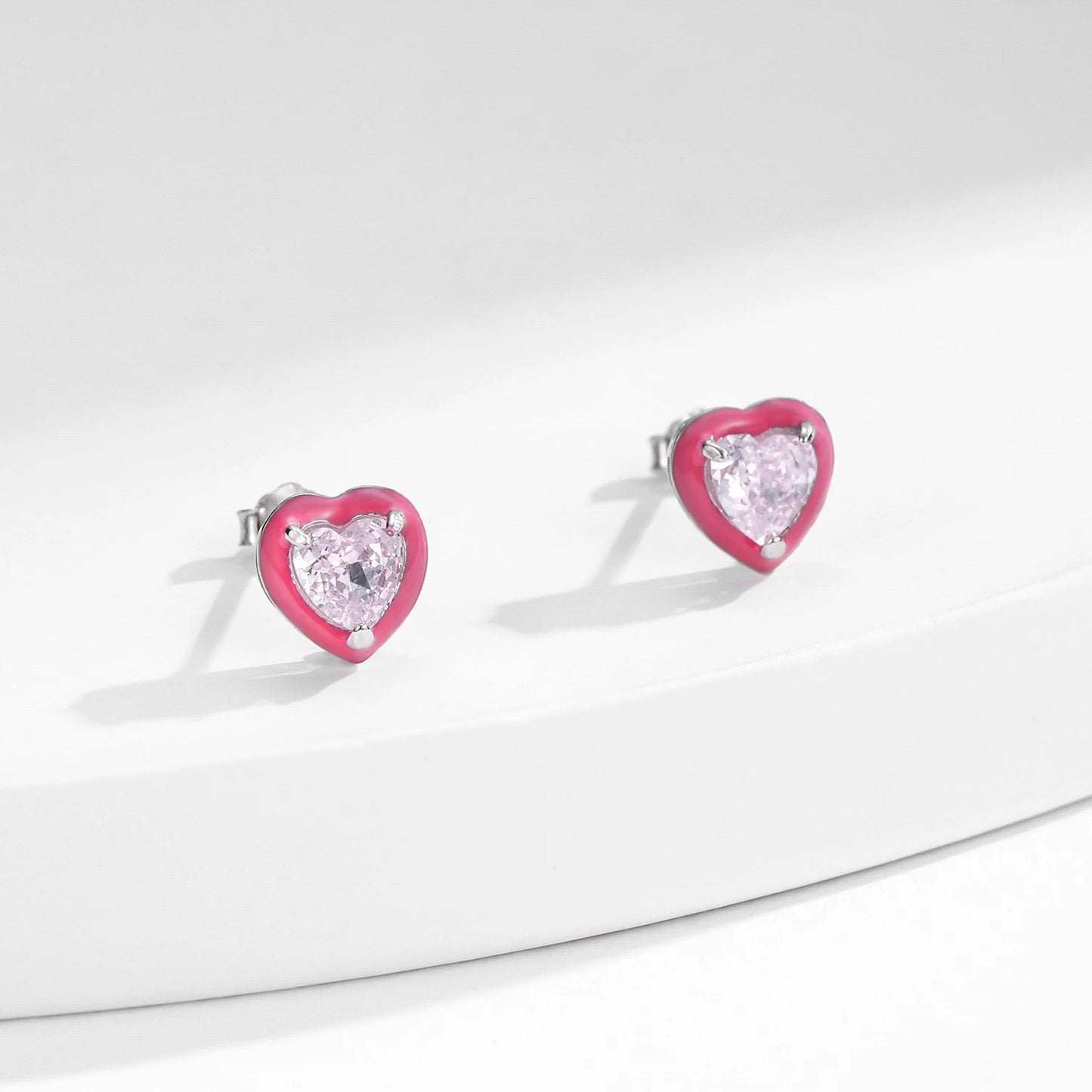 Stud earrings shaped like soft pink hearts, each set with a sparkling light pink heart-cut gemstone.

