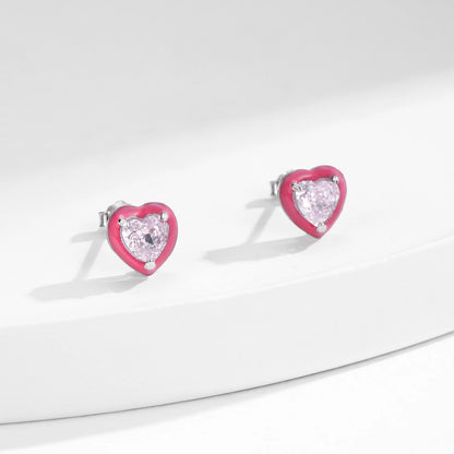 Stud earrings shaped like soft pink hearts, each set with a sparkling light pink heart-cut gemstone.

