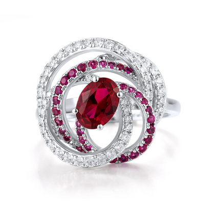 Vermiglio ring with a vivid red oval gemstone at the center, wrapped in spiraling bands of white and red stones set in silver.

