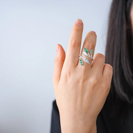 Adjustable silver ring featuring green marbled leaf accents in an open branch design.

