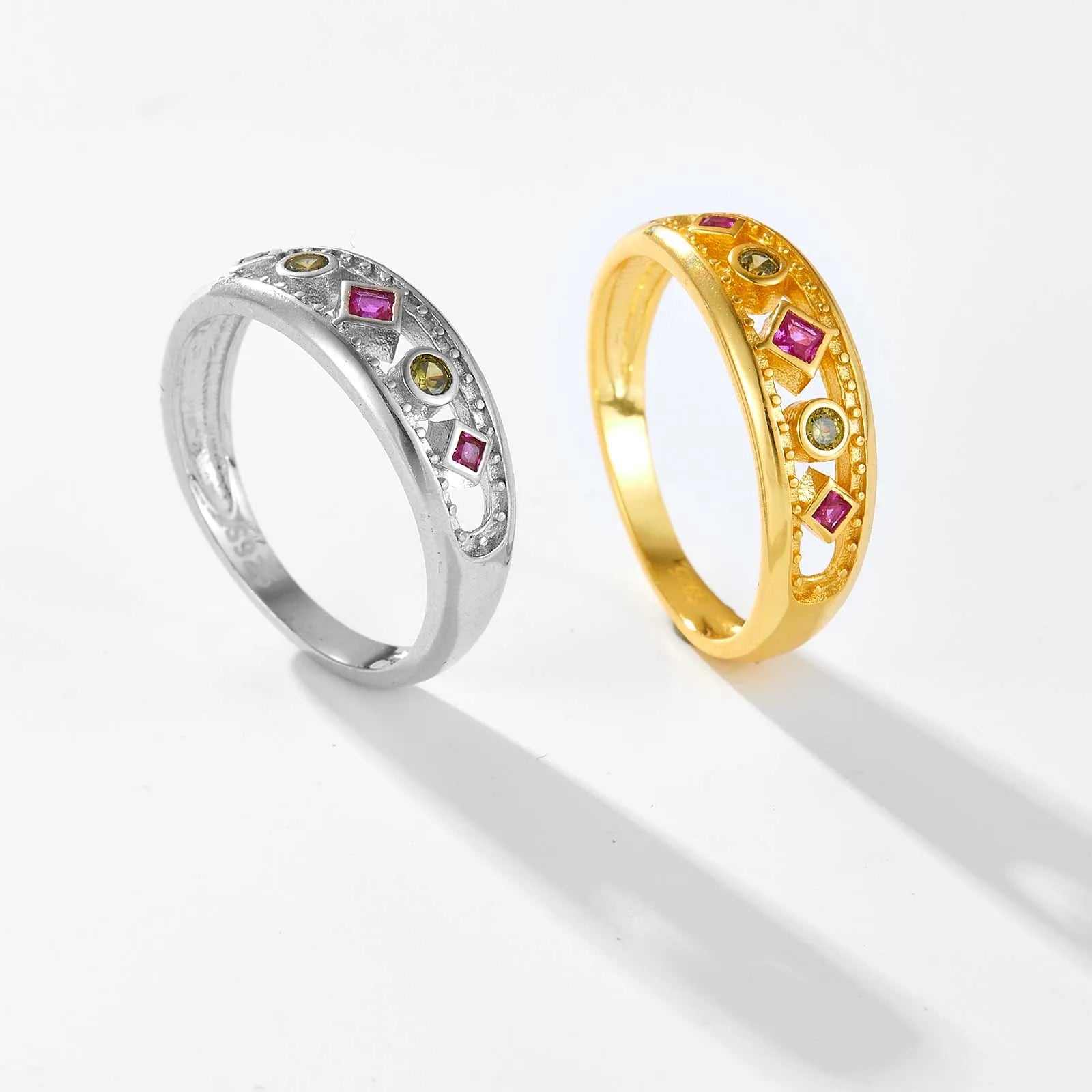 Gold ring with alternating pink square-cut and green round gemstones, framed by beaded detailing, displayed on a red background.


