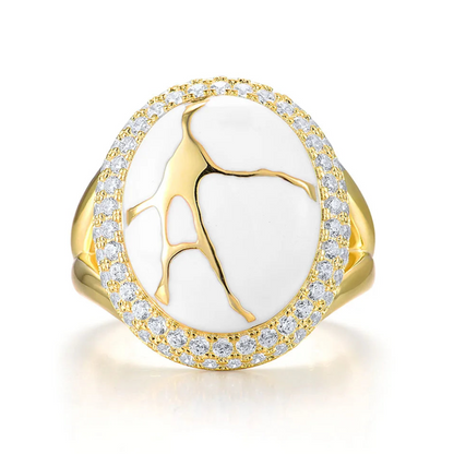 Gold ring with a large white stone featuring golden vein-like patterns, encircled by two rows of clear stones.

