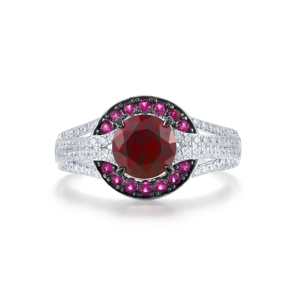 Silver ring with a large round red center stone, surrounded by a crescent of smaller pink stones and pavé white accents on a split band.

