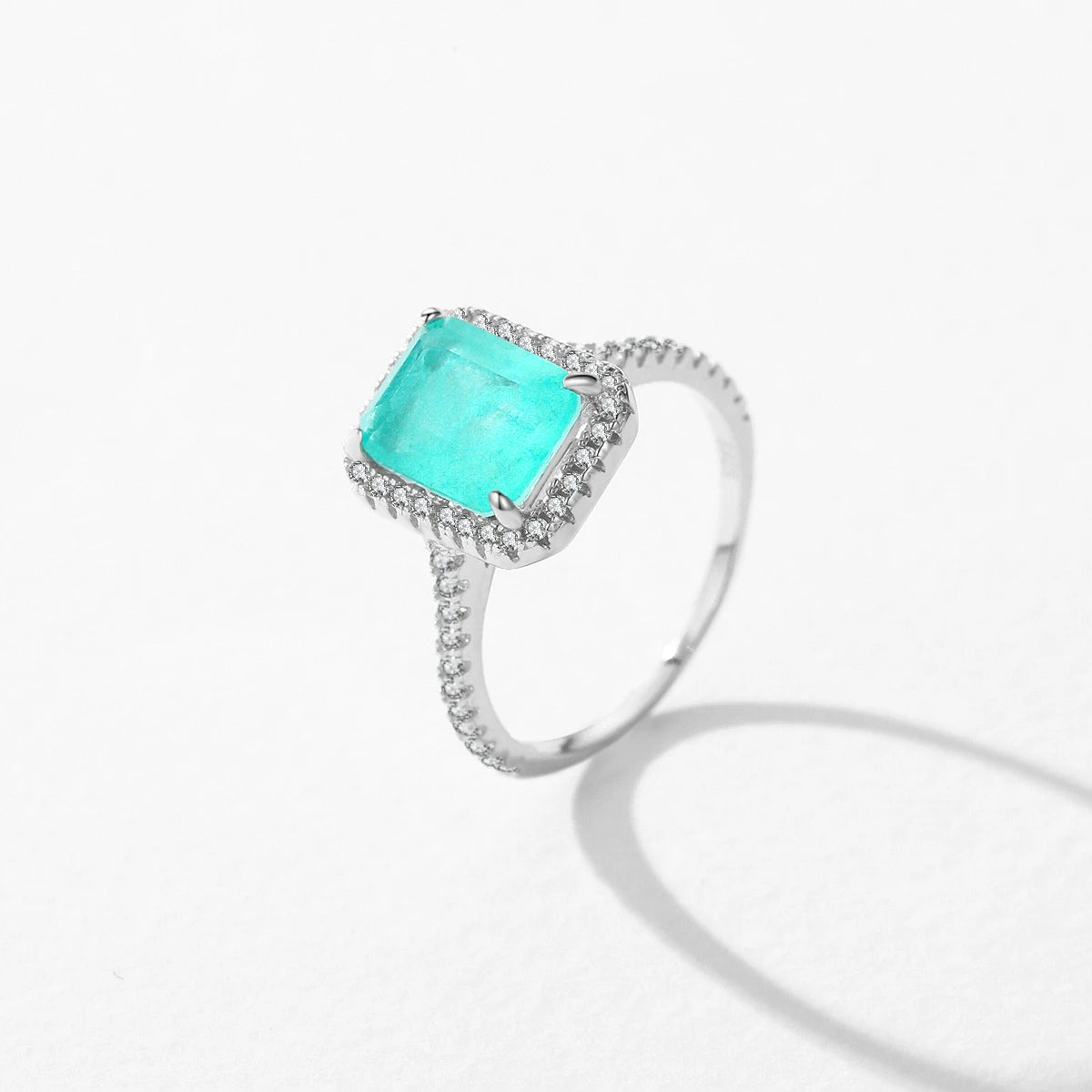 Rectangular green gemstone ring with a halo of clear stones on a silver band.

