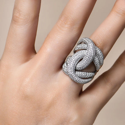 Wide silver ring with interlocking ribbon-like loops, entirely paved with sparkling white stones.

