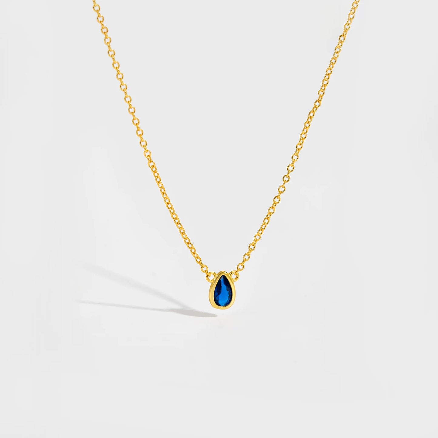 Gold chain necklace featuring a pear-shaped deep blue gemstone in a bezel setting