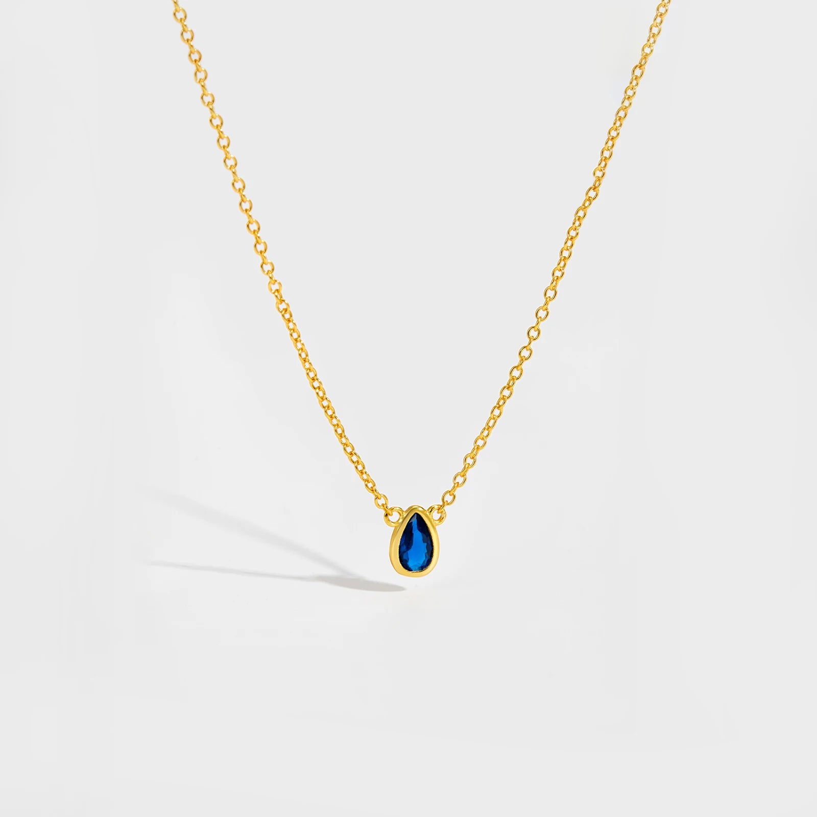 Gold chain necklace featuring a pear-shaped deep blue gemstone in a bezel setting