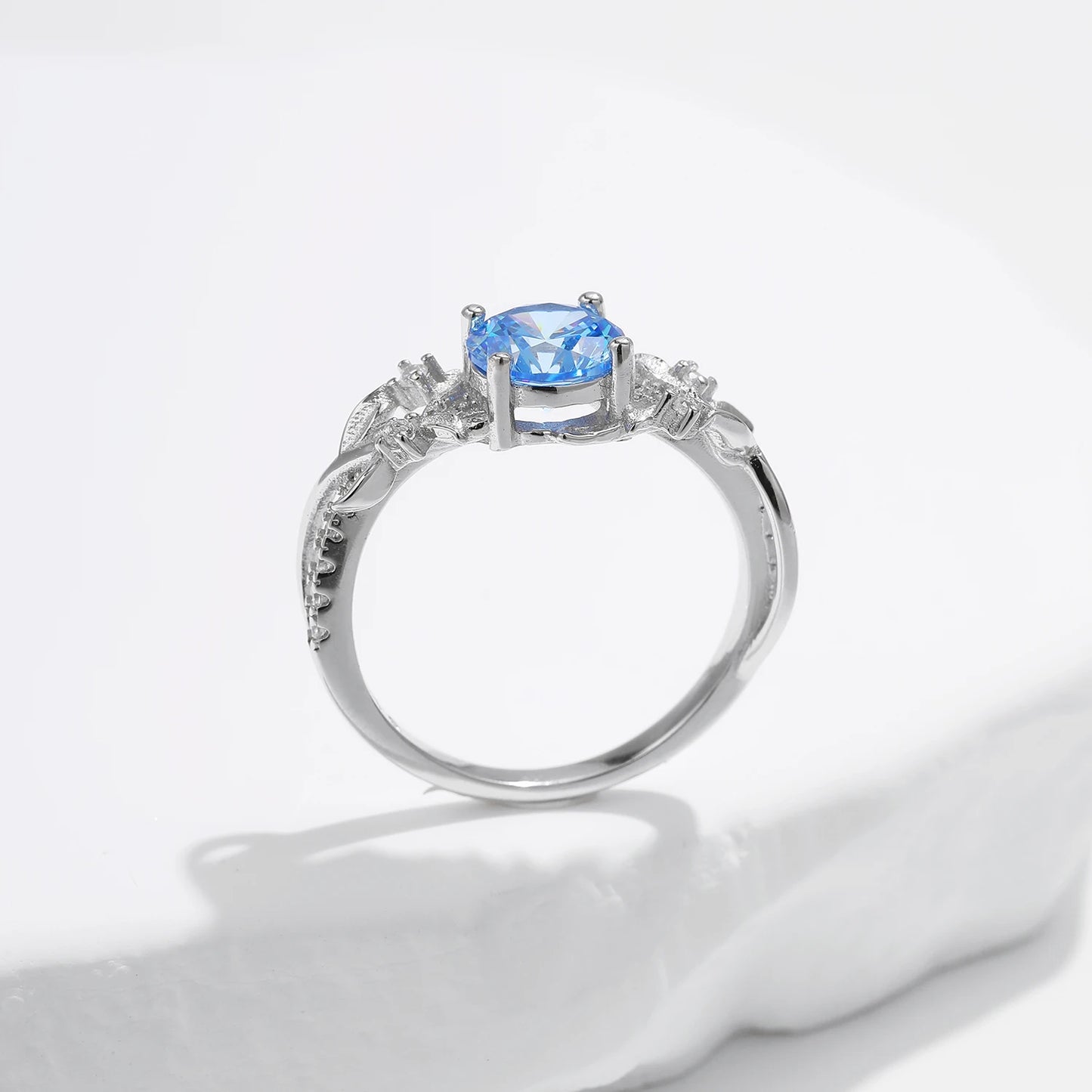 Sterling silver ring with a round sky blue gemstone and flowing leaf-like band details accented by small clear stones