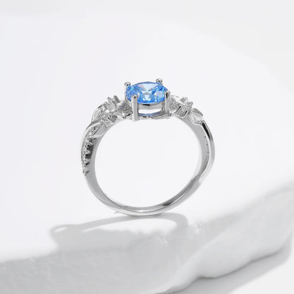 Sterling silver ring with a round sky blue gemstone and flowing leaf-like band details accented by small clear stones