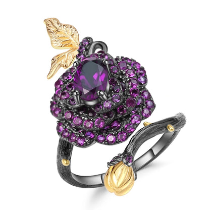 Black rose ring with layered red gemstones, accented by a gold leaf and bud on a dark branch-like band.

