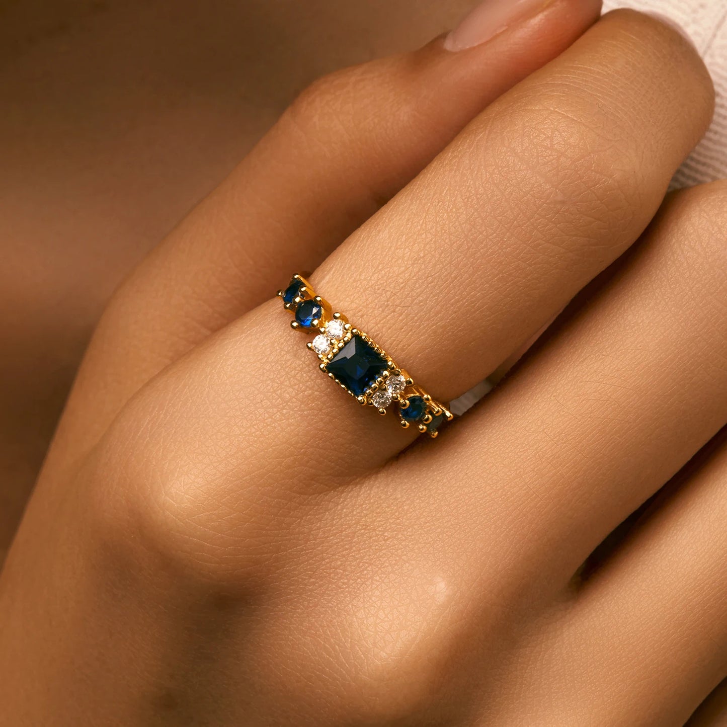 Gold-plated sterling silver ring with a central square-cut deep blue stone and surrounding clear round stones

