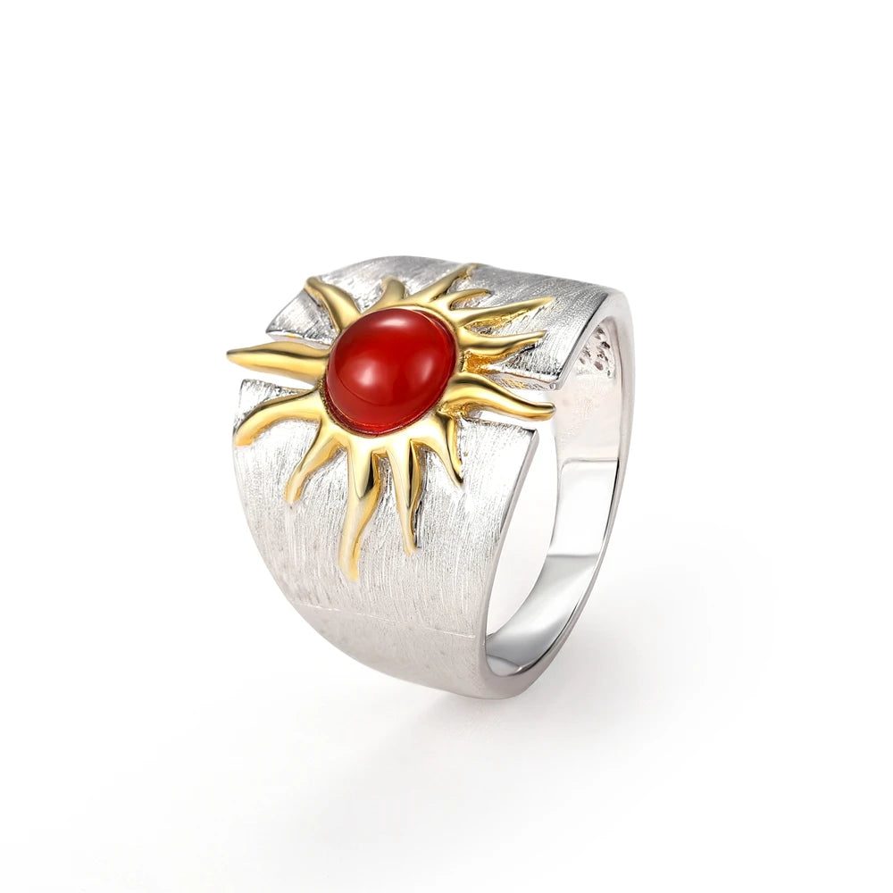 Wide silver ring with a central red cabochon framed by gold sun-ray detailing.

