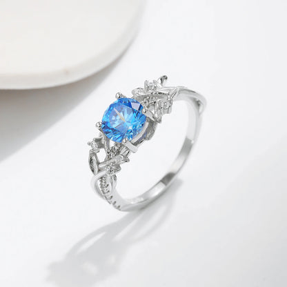 Sterling silver ring with a round sky blue gemstone and flowing leaf-like band details accented by small clear stones