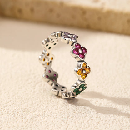 Silver ring with multicoloured four-petal flower gemstones set around the band.

