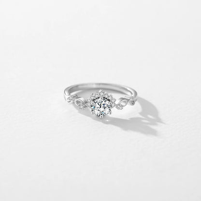 Silver ring with a central round-cut stone surrounded by delicate side diamonds and twisted vine-like detailing.

