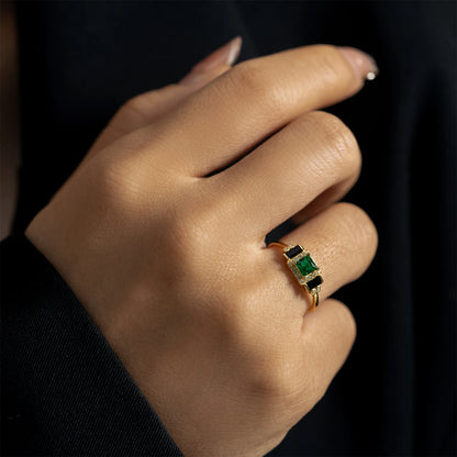 Gold ring with square green center stone, black accents, and pavé border

