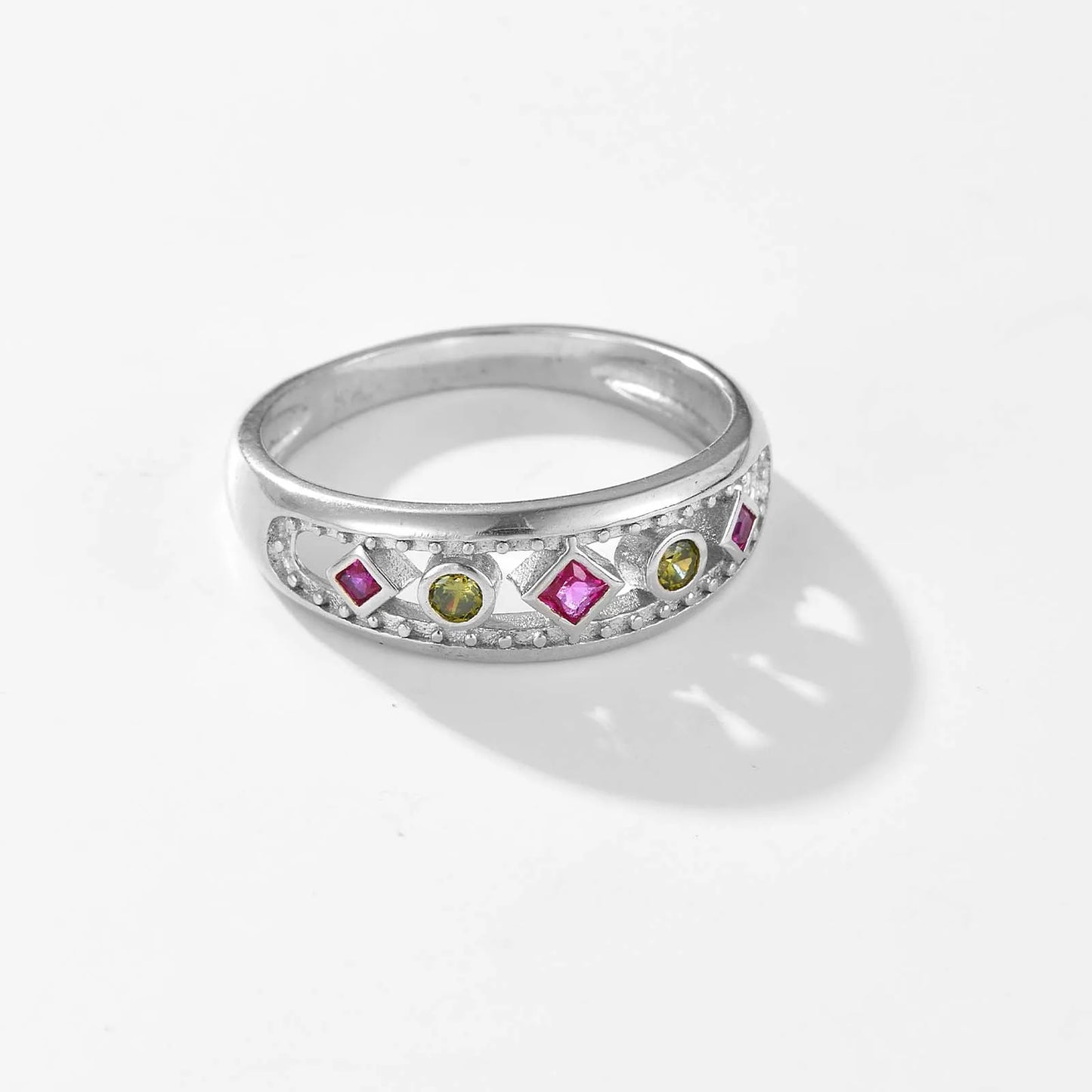 Gold ring with alternating pink square-cut and green round gemstones, framed by beaded detailing, displayed on a red background.

