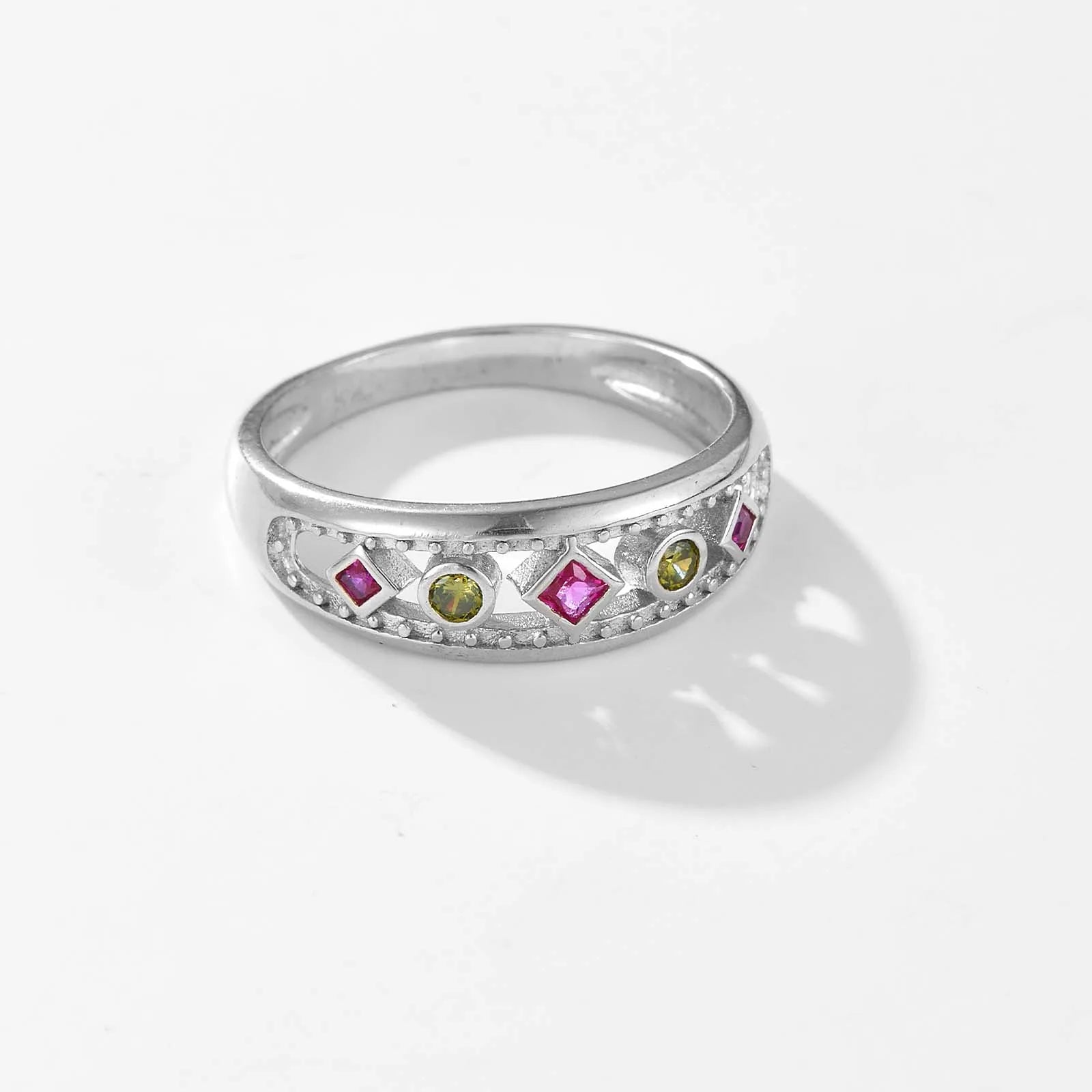 Gold ring with alternating pink square-cut and green round gemstones, framed by beaded detailing, displayed on a red background.

