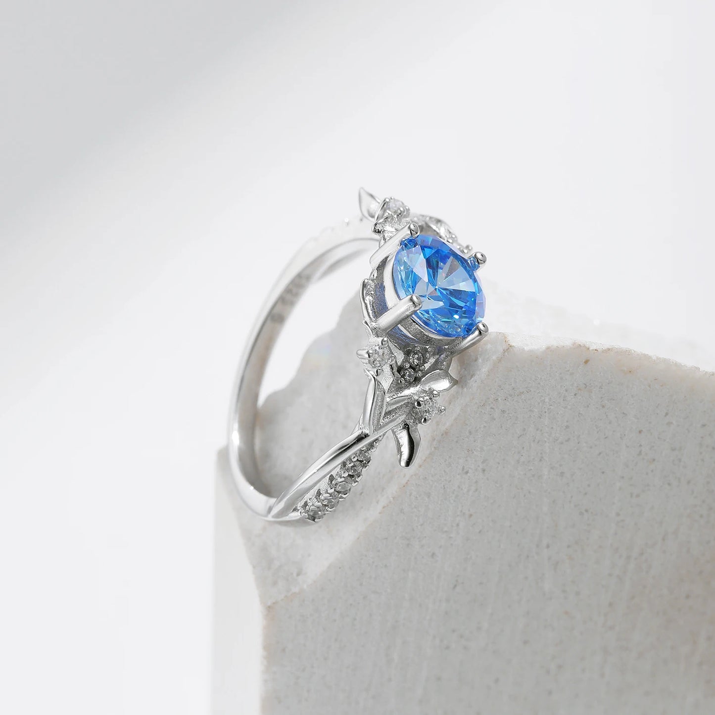Sterling silver ring with a round sky blue gemstone and flowing leaf-like band details accented by small clear stones