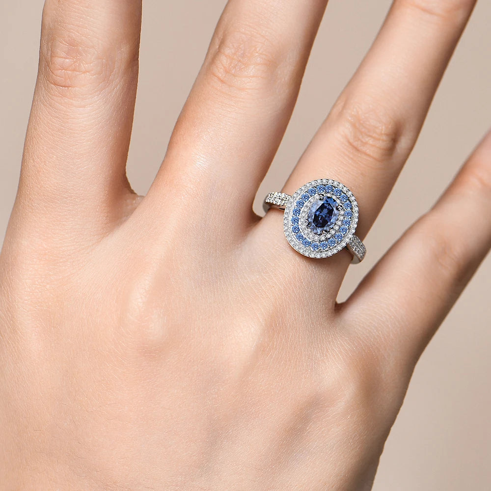 Sterling silver ring with an oval-cut deep blue gemstone surrounded by two concentric halos of white and blue stones, set on a pavé band