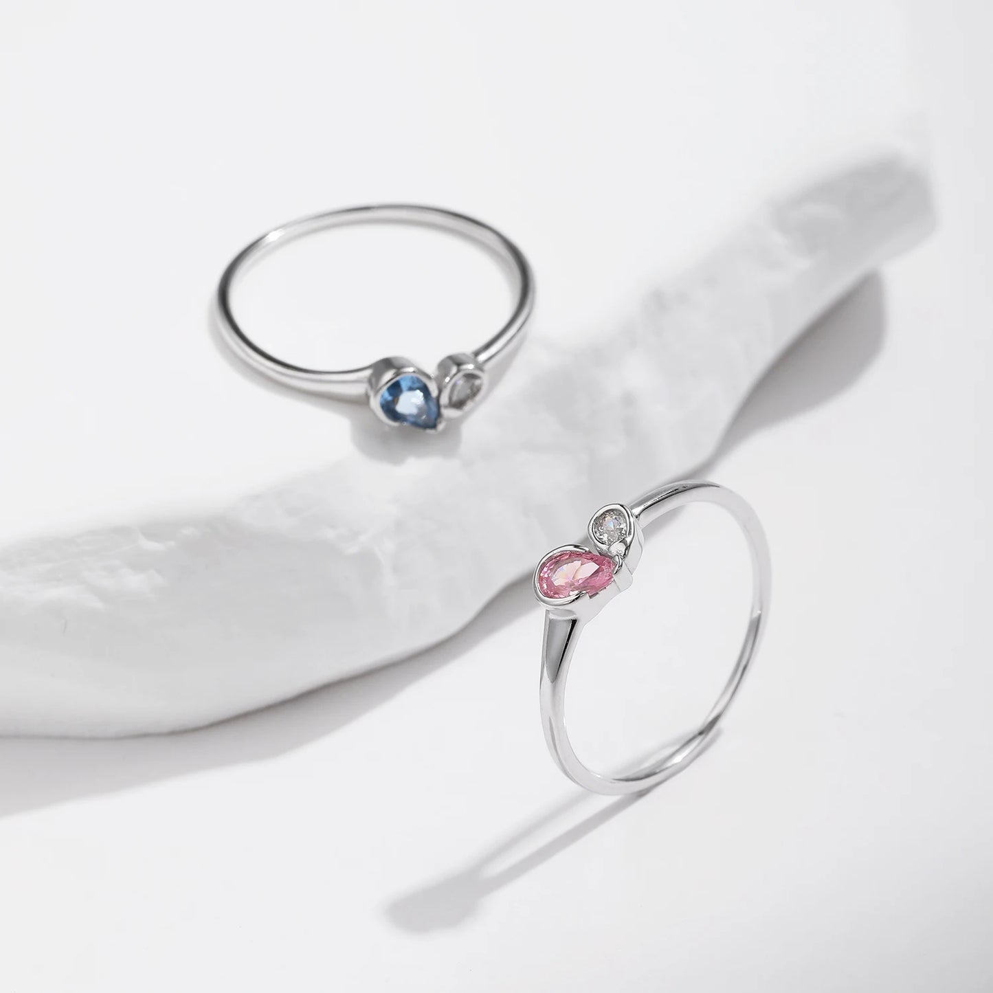 Sterling silver ring with a pear-shaped blue stone and round white stone set side by side
Sterling silver ring featuring a pink teardrop stone paired with a round clear stone in an open-heart inspired setting.


