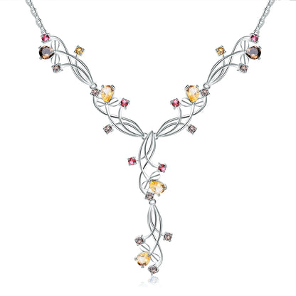 Silver necklace with an intricate swirling design, adorned with multicolored gemstones in pink, yellow, brown, and clear tones.

