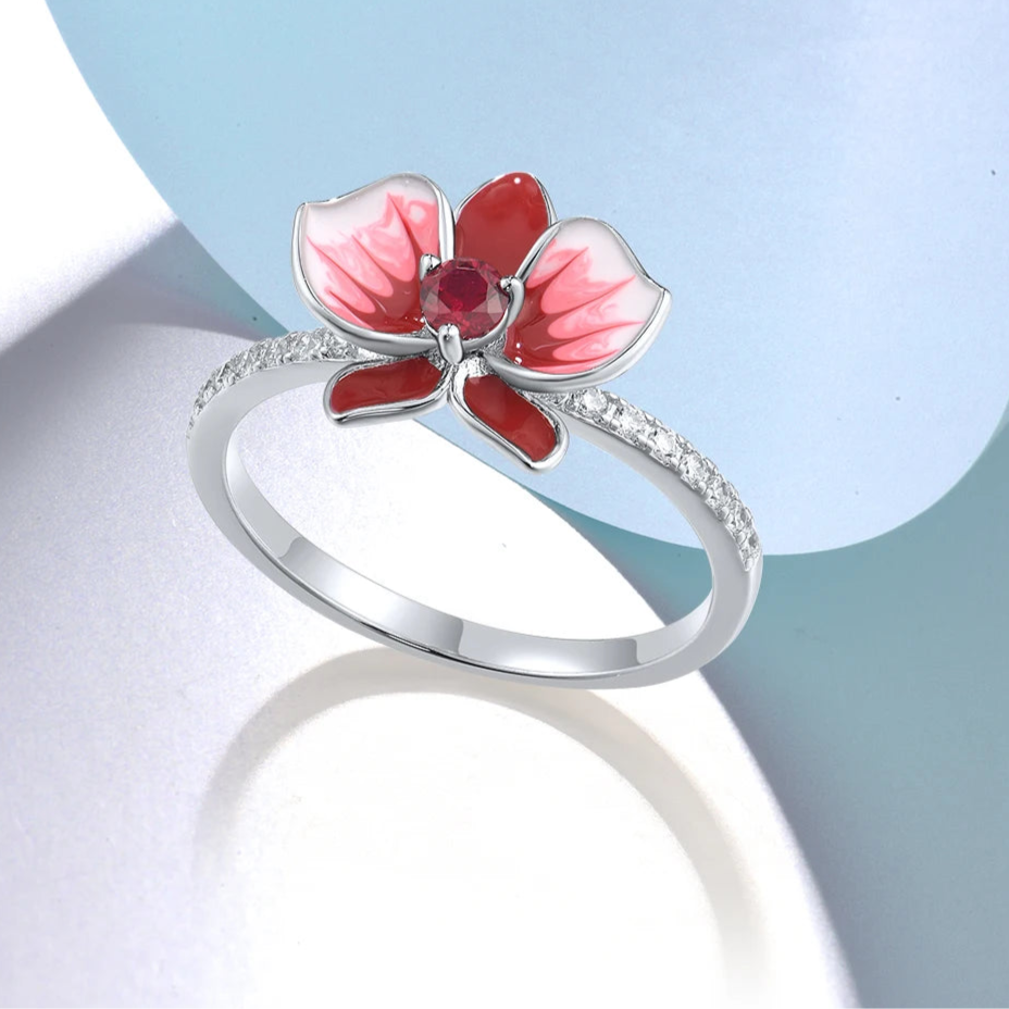 Silver floral ring featuring a red and white enamel orchid with a central ruby-colored stone.

