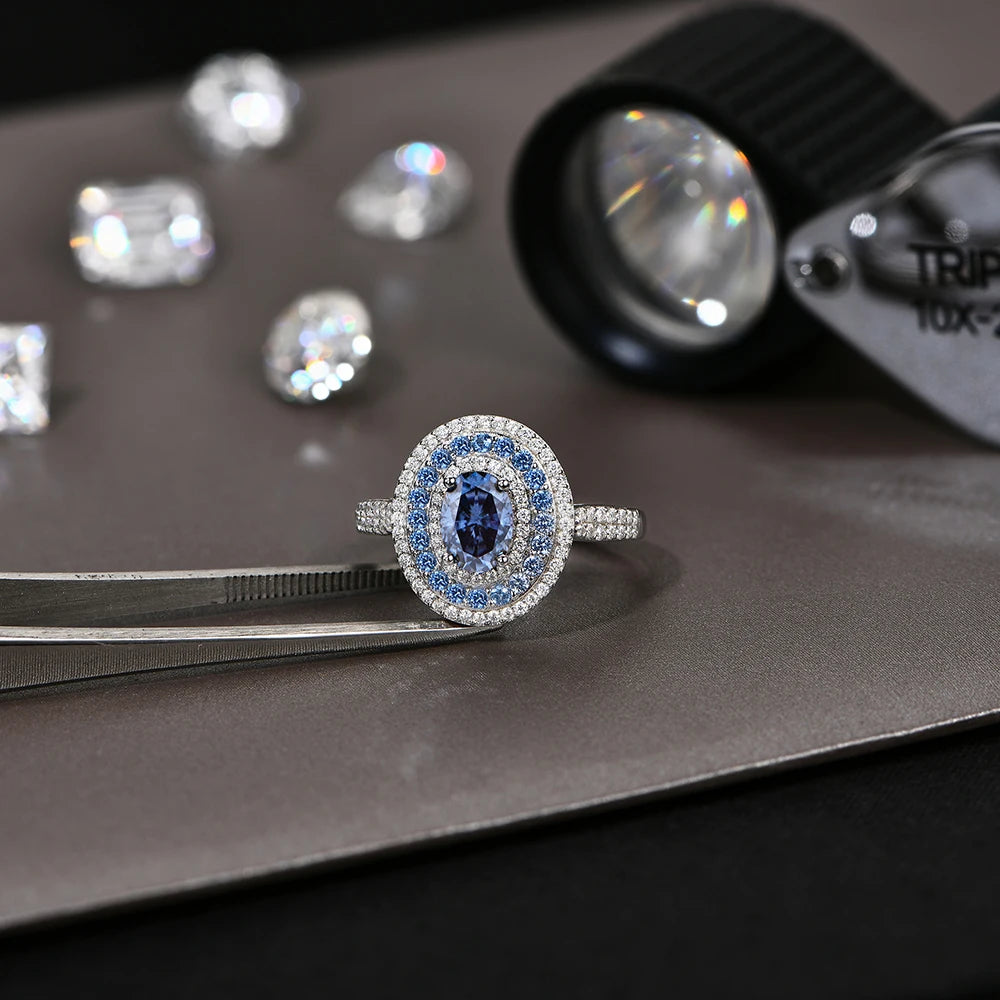 Sterling silver ring with an oval-cut deep blue gemstone surrounded by two concentric halos of white and blue stones, set on a pavé band