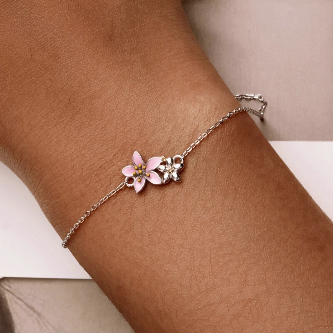 Delicate silver bracelet featuring two small pink cherry blossom charms on a fine chain.

