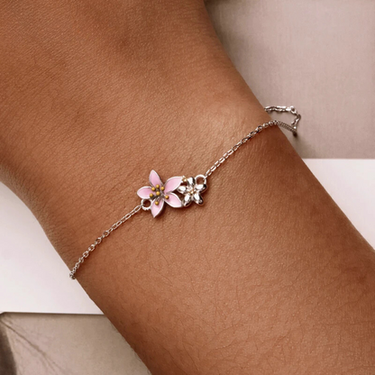 Delicate silver bracelet featuring two small pink cherry blossom charms on a fine chain.

