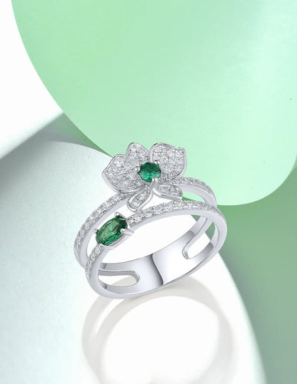 Silver ring featuring a sparkling orchid flower design with green and clear stones and a double-band setting

